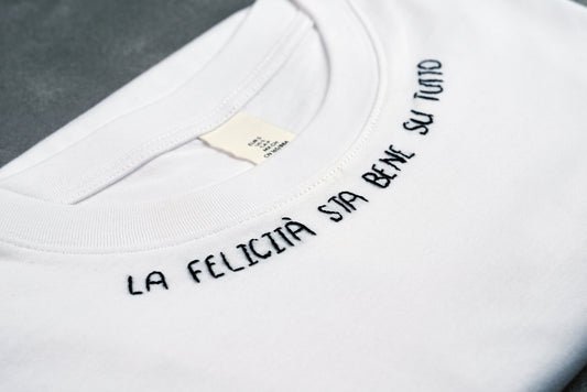 Dettaglio T-shirt “LA FELICITÀ STA BENE SU TUTTO”, la maglietta in 100% cotone è ricamata con la scritta "la felicità sta bene su tutto"
