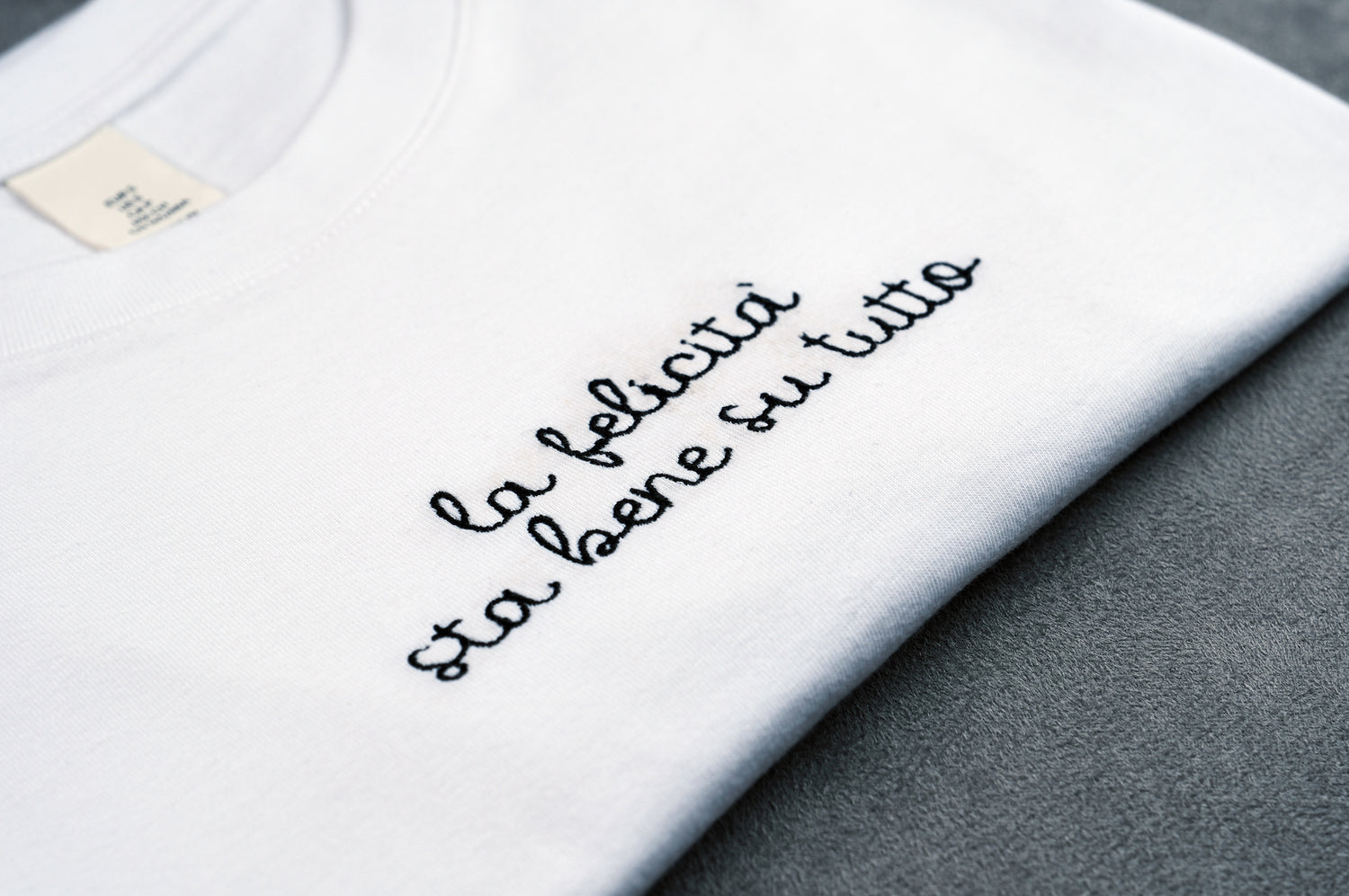 Dettaglio T-shirt “LA FELICITÀ STA BENE SU TUTTO”, la maglietta in 100% cotone è ricamata con la scritta "la felicità sta bene su tutto"