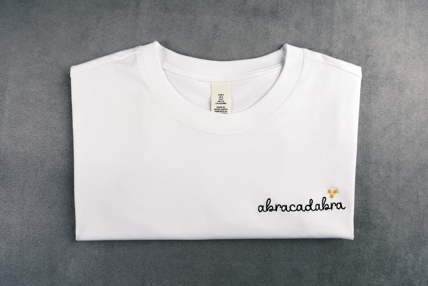 Dettaglio della T-shirt “ABRACADABRA”, la maglietta in 100% cotone è ricamata con la scritta "abracadabra"