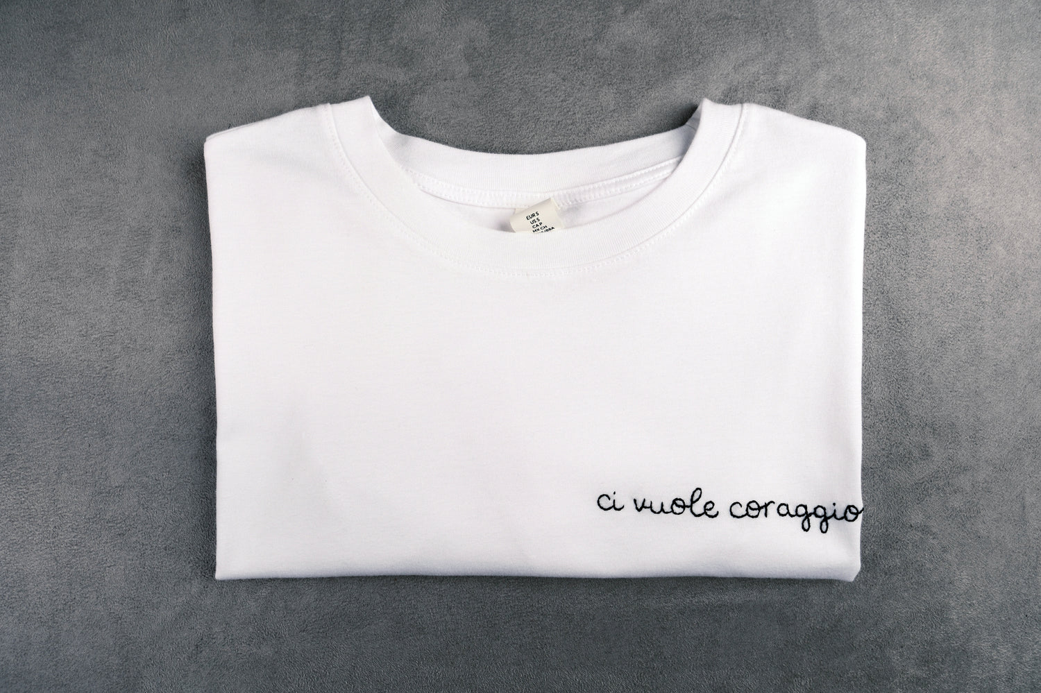 Dettaglio della T-shirt “CI VUOLE CORAGGIO”, la maglietta in 100% cotone è ricamata con la scritta "ci vuole coraggio"